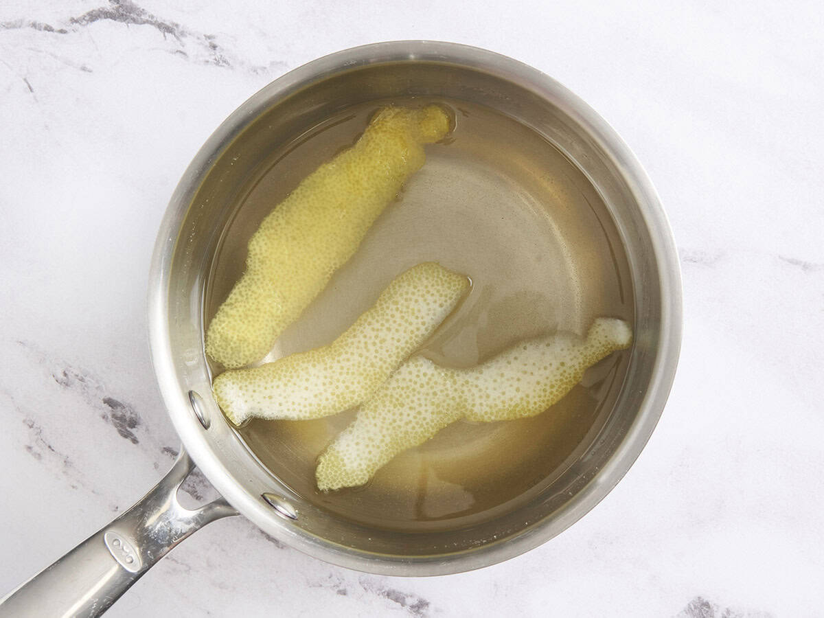 Cooled simple syrup with lemon peels in a sauce pan.