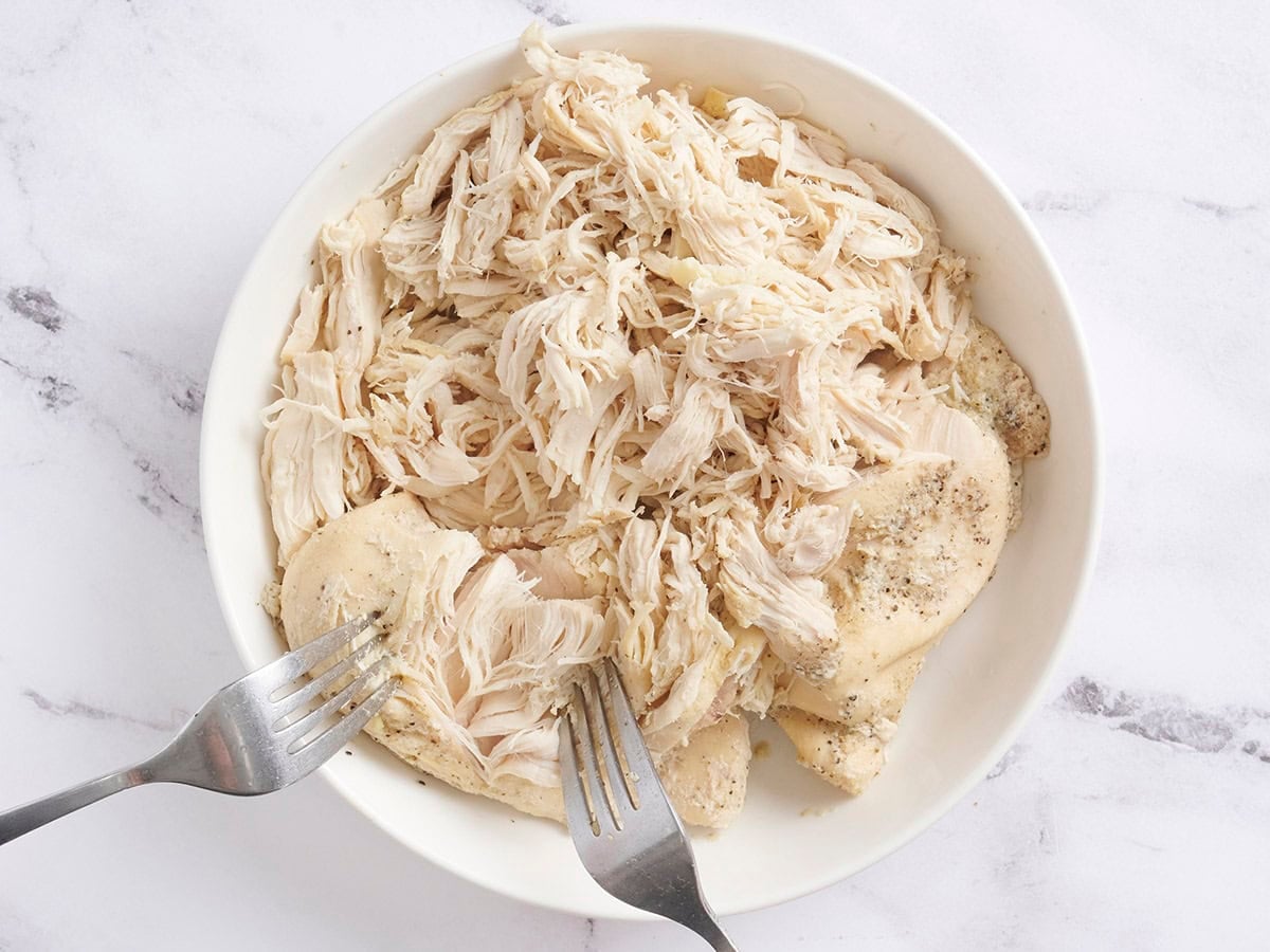 Two forks shredded chicken breasts on a plate.