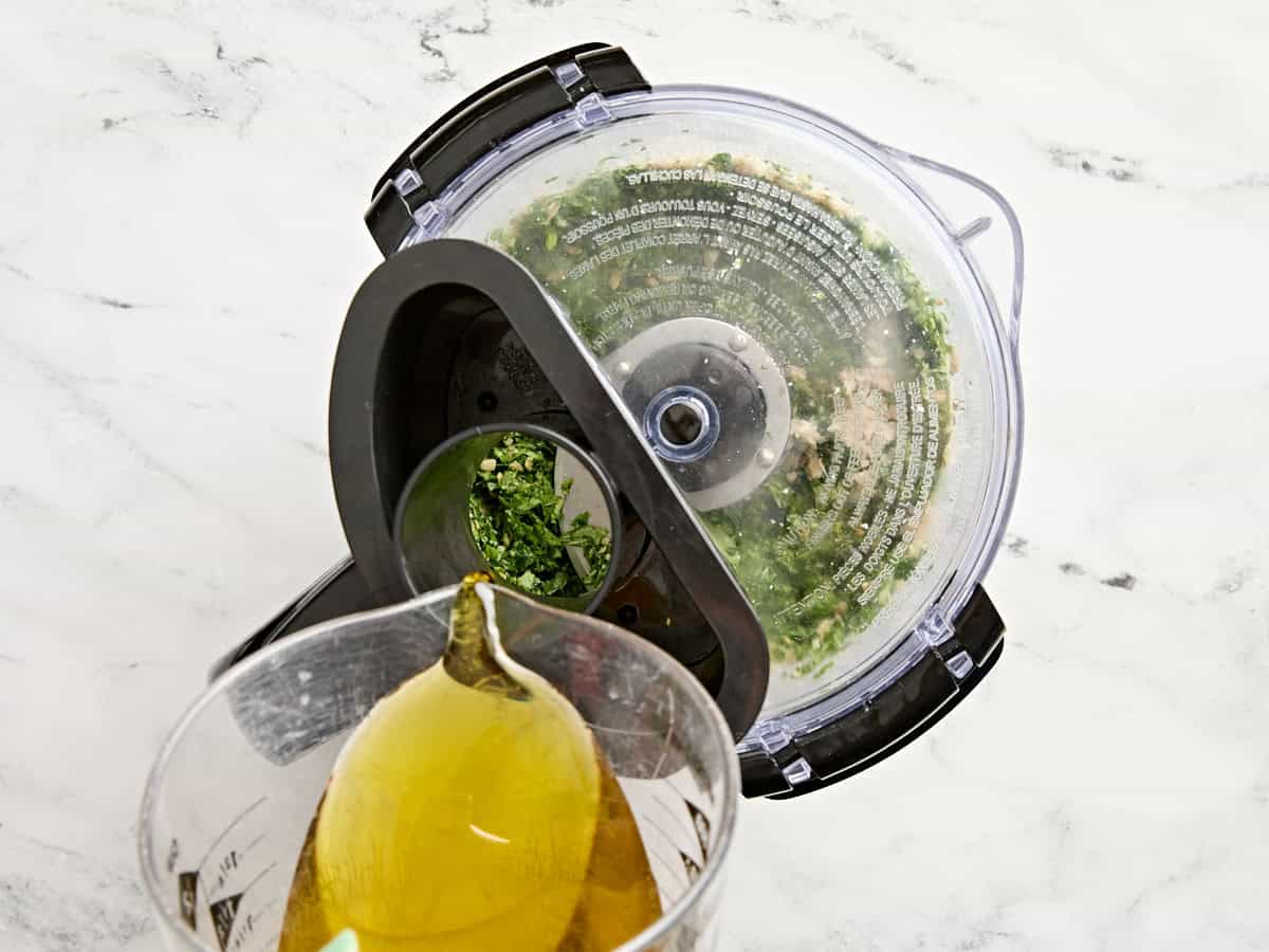 Olive oil being streamed into a food processor of budget friendly pesto.
