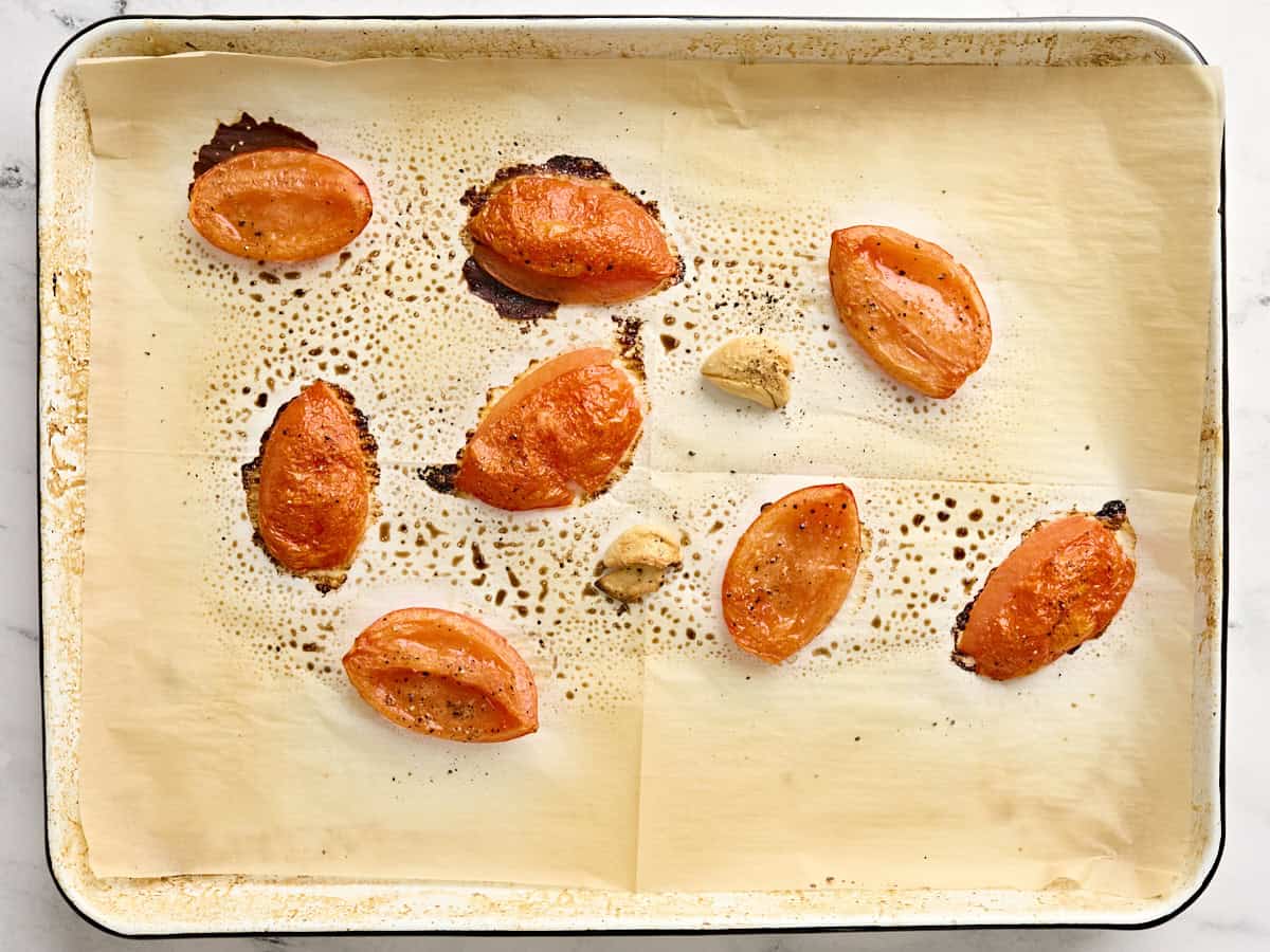 Roasted tomato flesh and crushed garlic cloves on a baking sheet.
