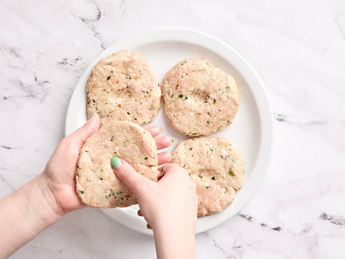 Hands forming chicken burger patties.