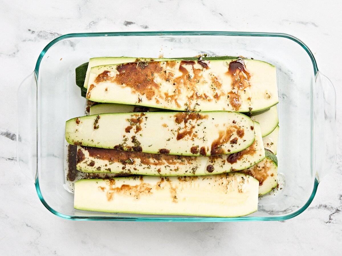 Fresh zucchini slices in a marinade in a glass dish.