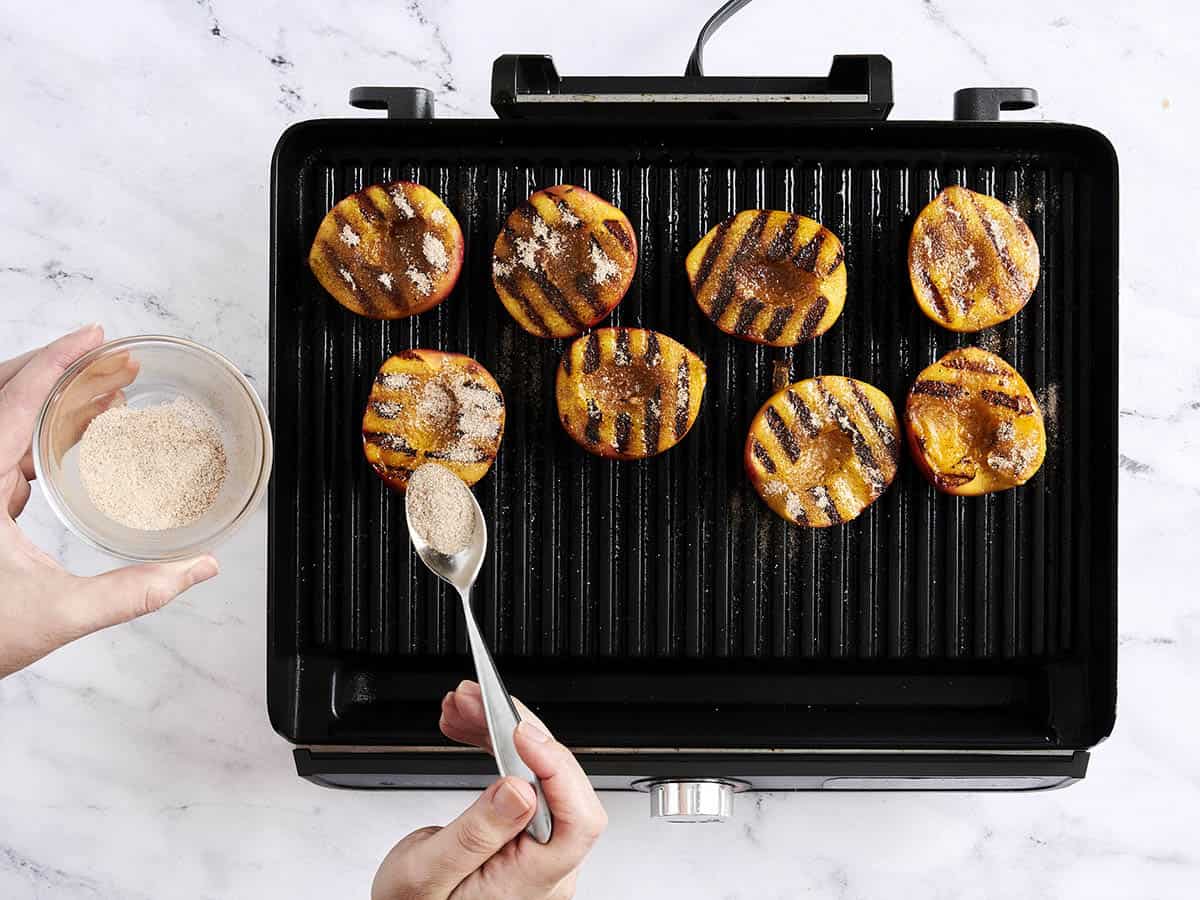 A spoon sprinkling cinnamon sugar over grilled peaches.