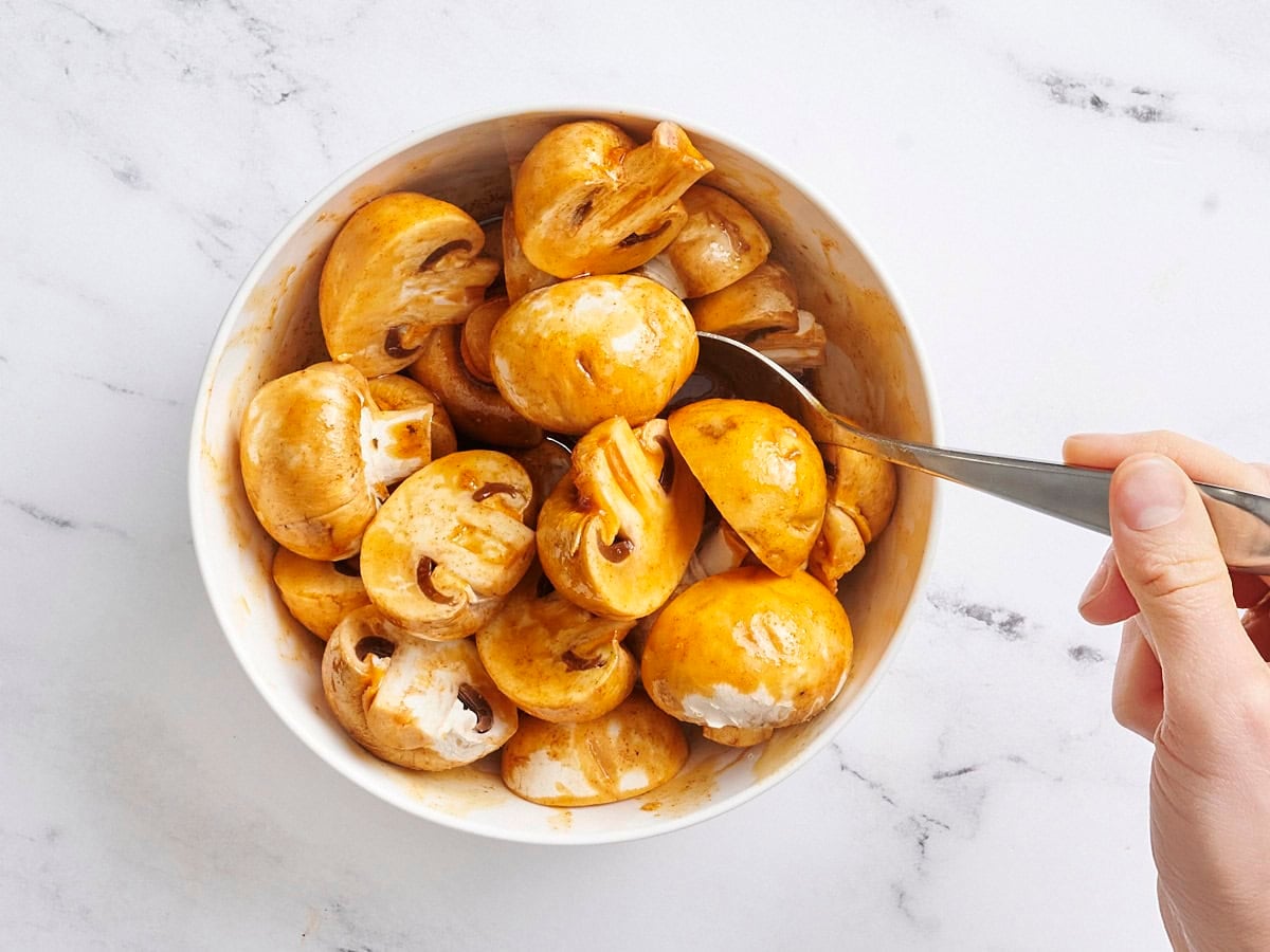 Sliced white mushrooms being tossed in a homemade marinade.