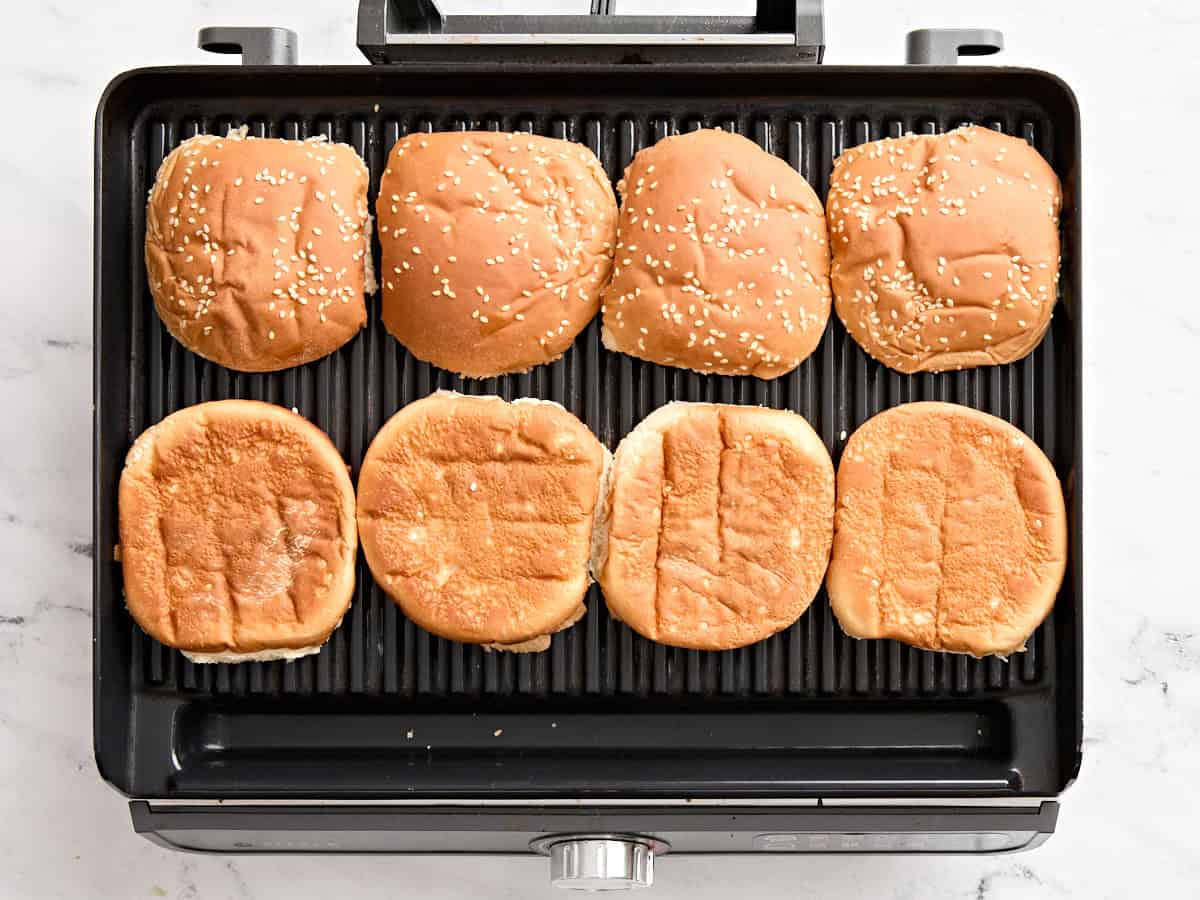Burger buns toasting on a grill.