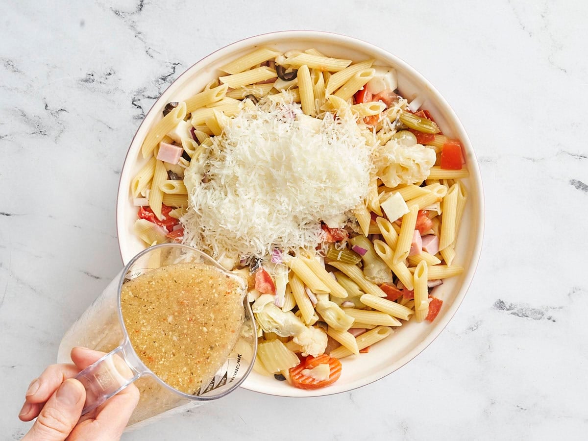 Shredded parmesan and italian dressing added to antipasto salad in a bowl.