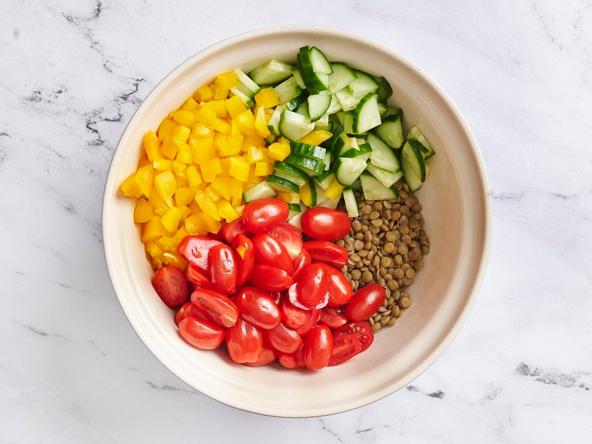Cooked lentils, plum tomatoes, yellow bell pepper, and cucumber in a bowl.