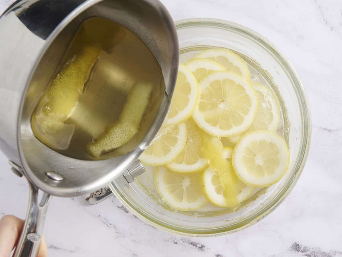 Lemon slices in a punch bowl with simple syrup being poured over.