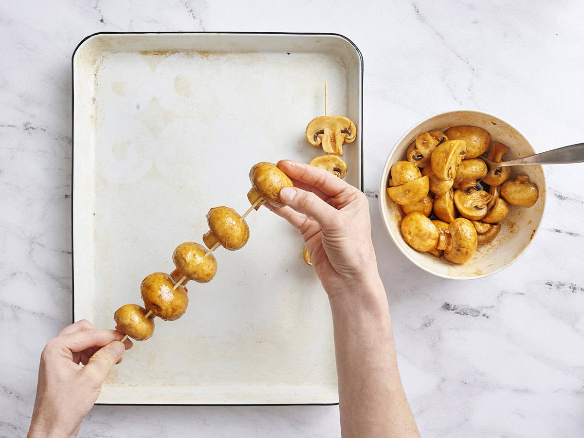 Marinated mushrooms being threaded onto wooden skewers.
