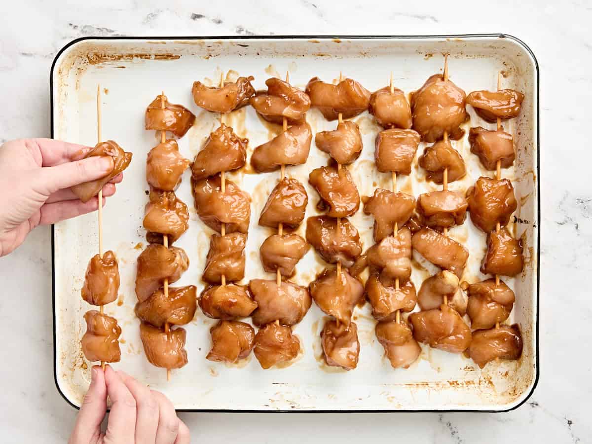 Marinated diced chicken being placed on skewers.