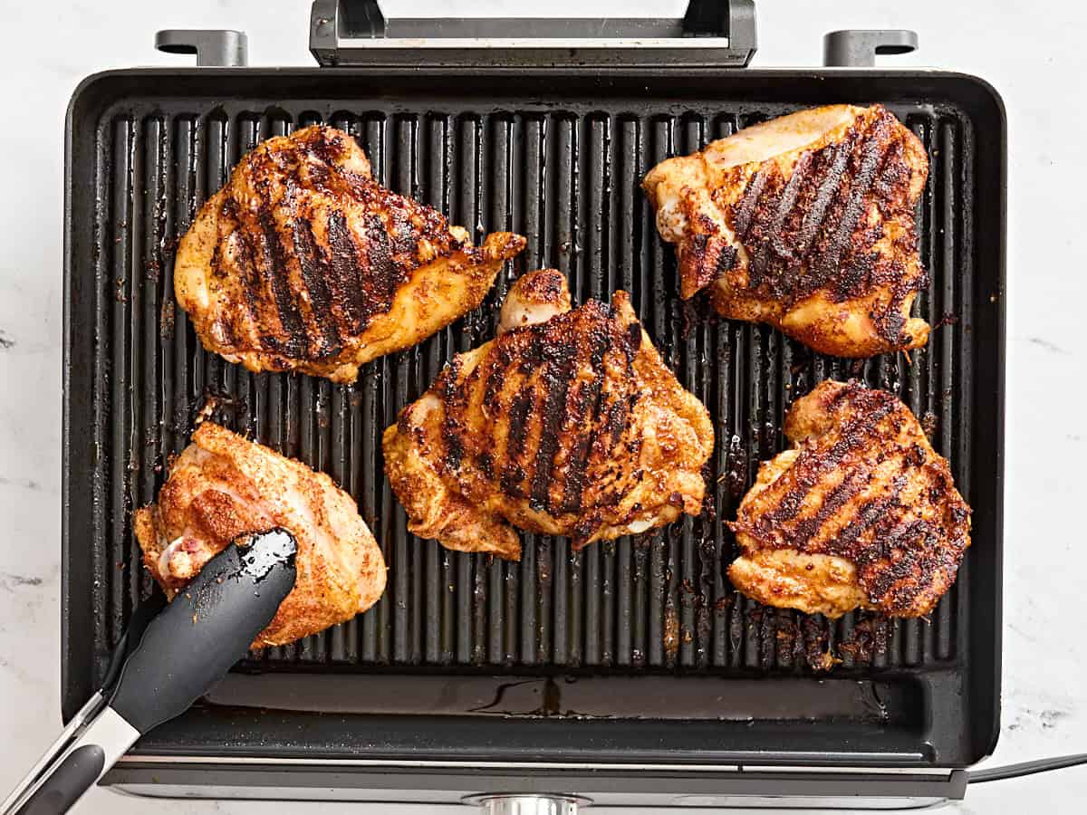 Kitchen tongs flipping over grilled thighs.