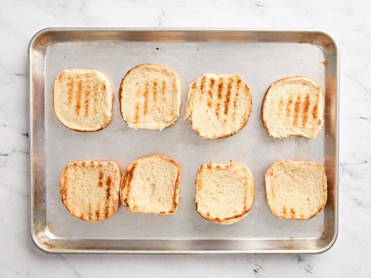 Toasted burger buns on a baking sheet.