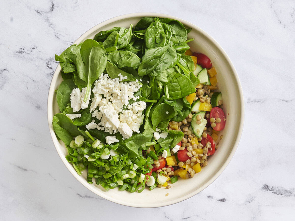 Spinach, feta, and sliced green onions added to a bowl of lentil salad.