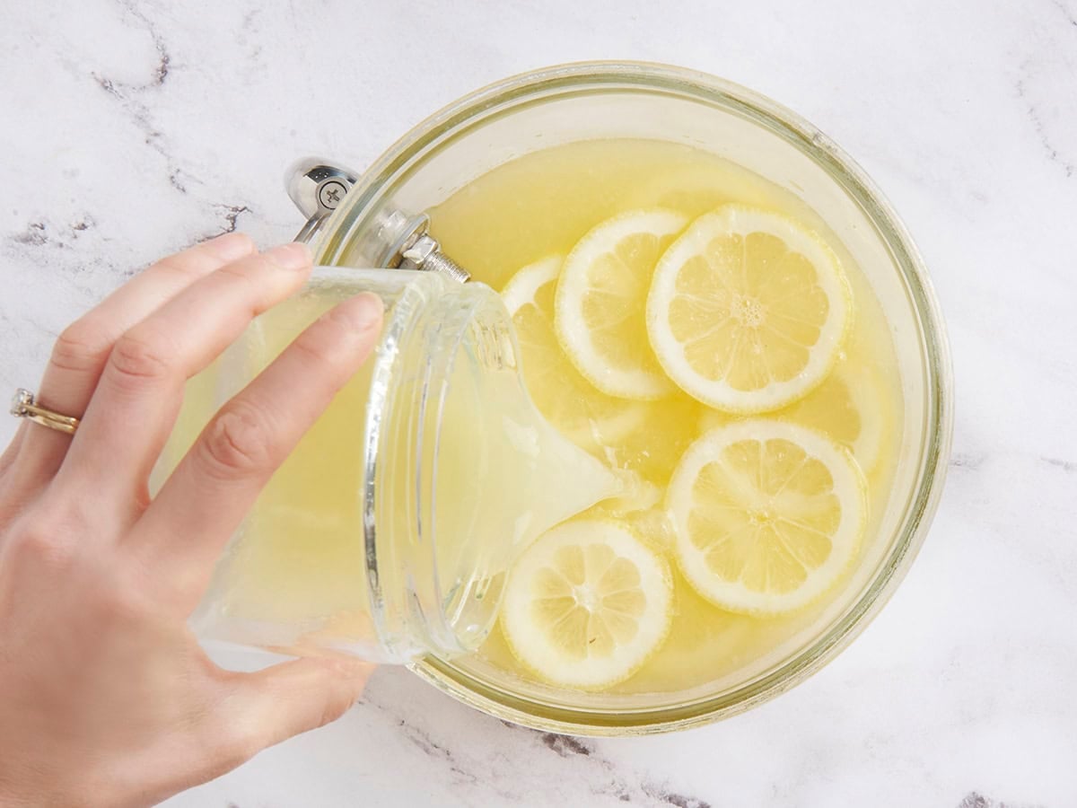 Lemon juice being poured into homemade lemonade in a punch bowl.