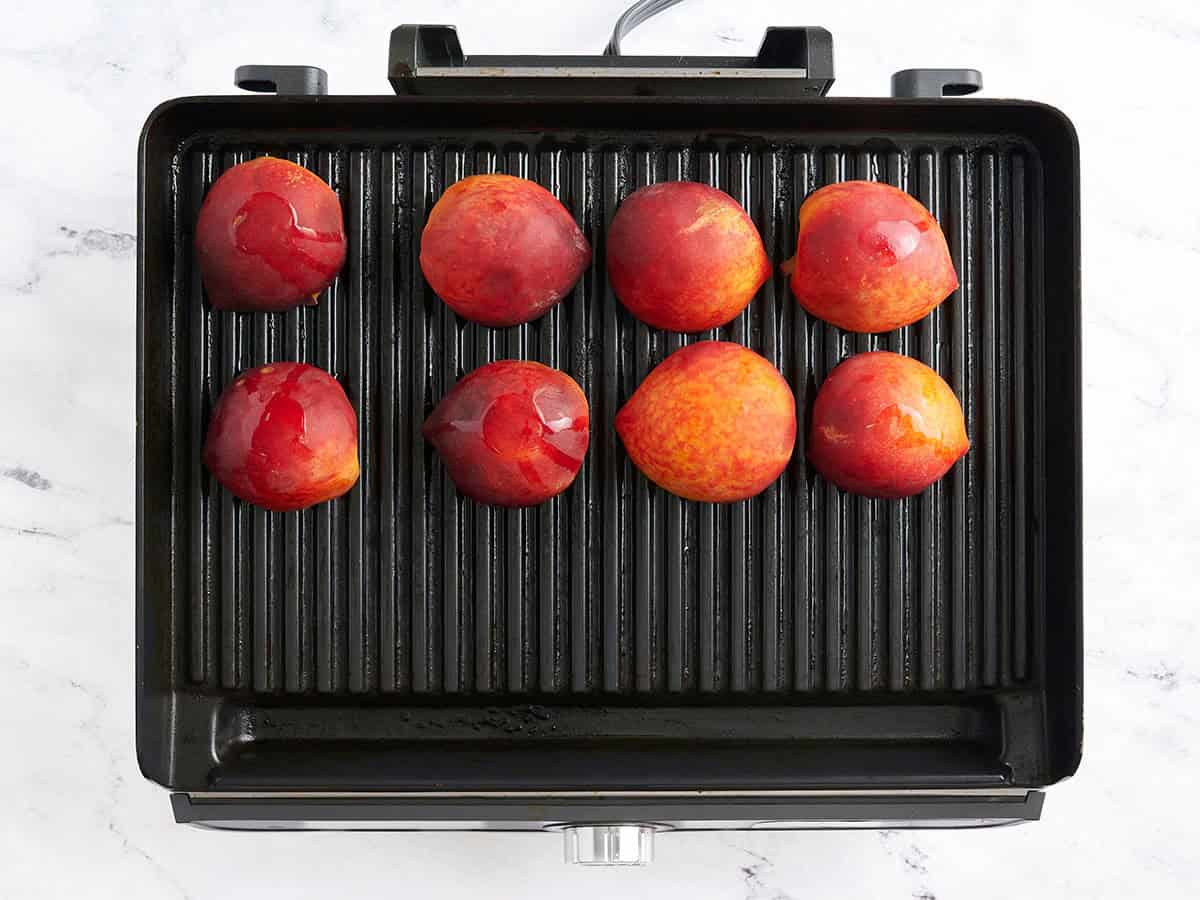 Peach halves grilling on a grill.
