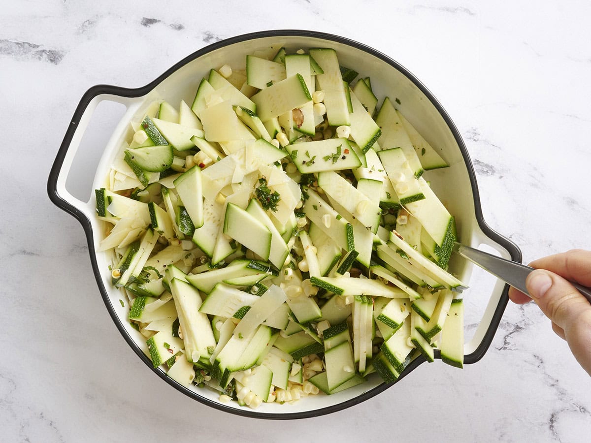 Zucchini, corn and toasted almond salad being tossed with the dressing.