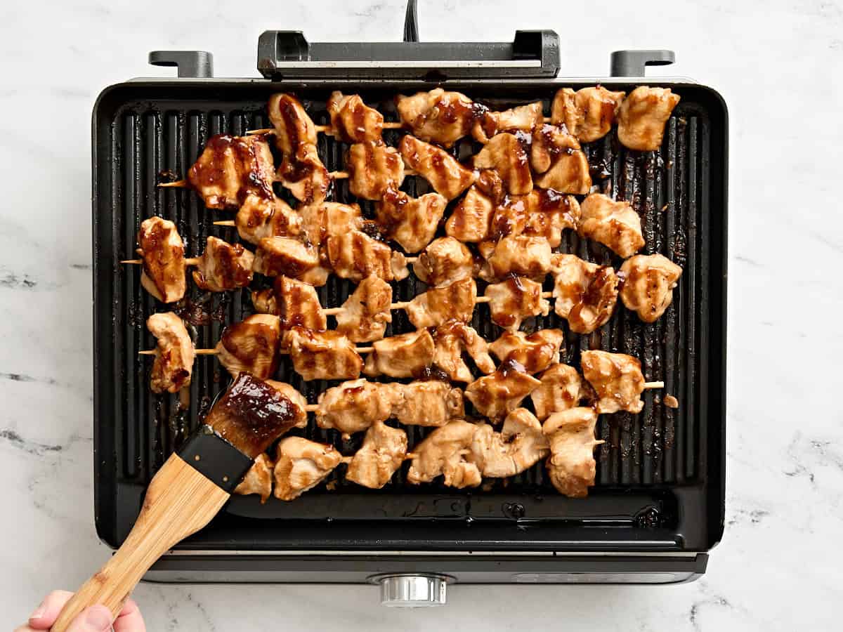 Grilled chicken kebabs being brushed with teriyaki sauce.