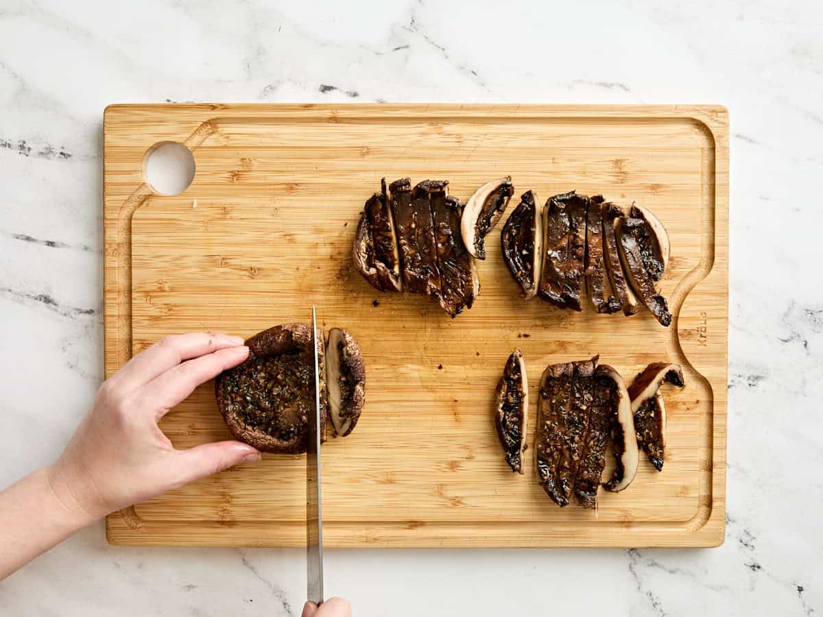 A knife slicing baked portabella mushrooms into slices.