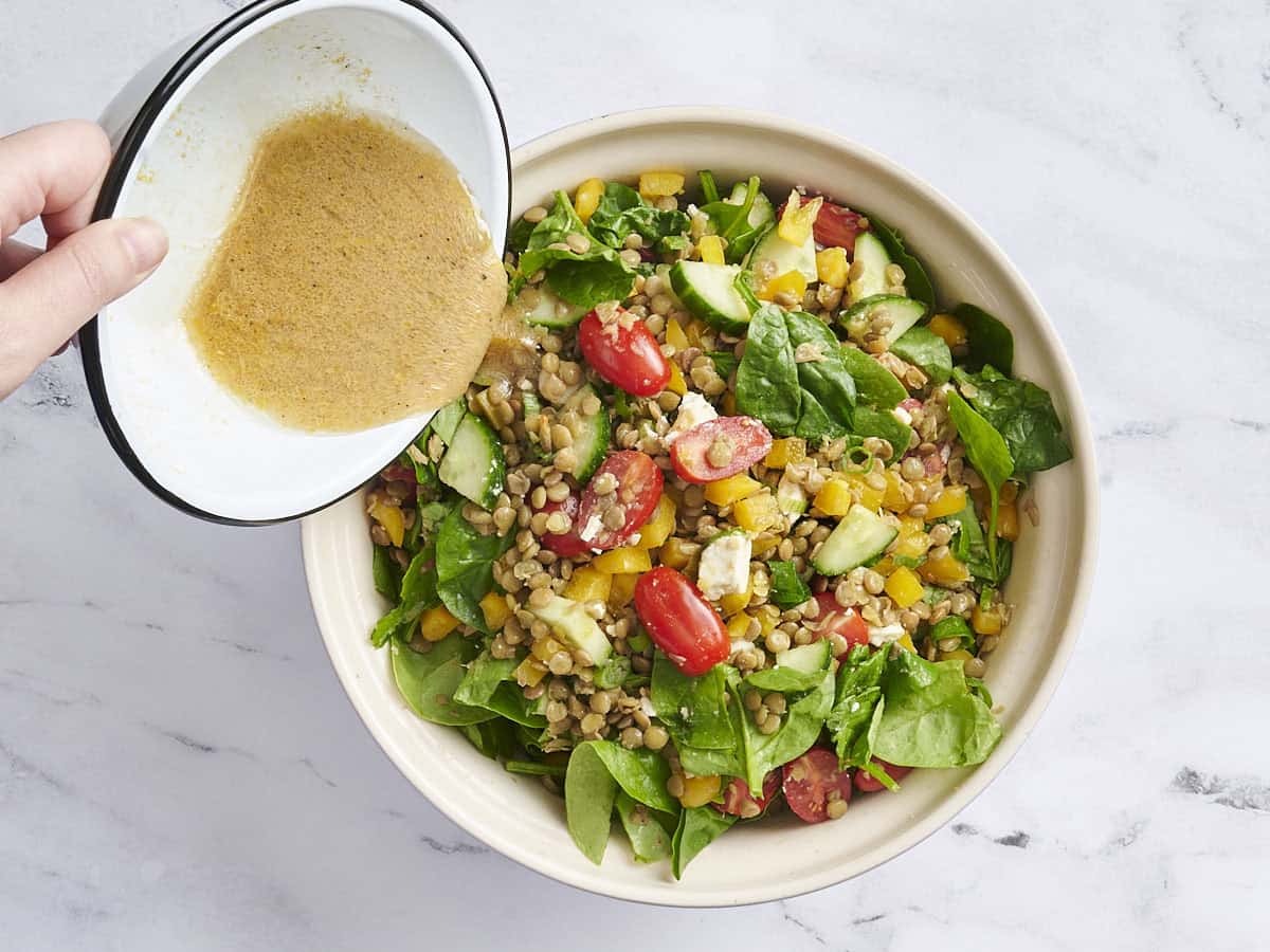 A homemade vinaigrette being poured into a bowl of lentil salad.
