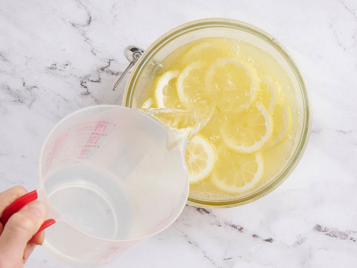 Cold water being poured into homemade lemonade in a punch bowl.