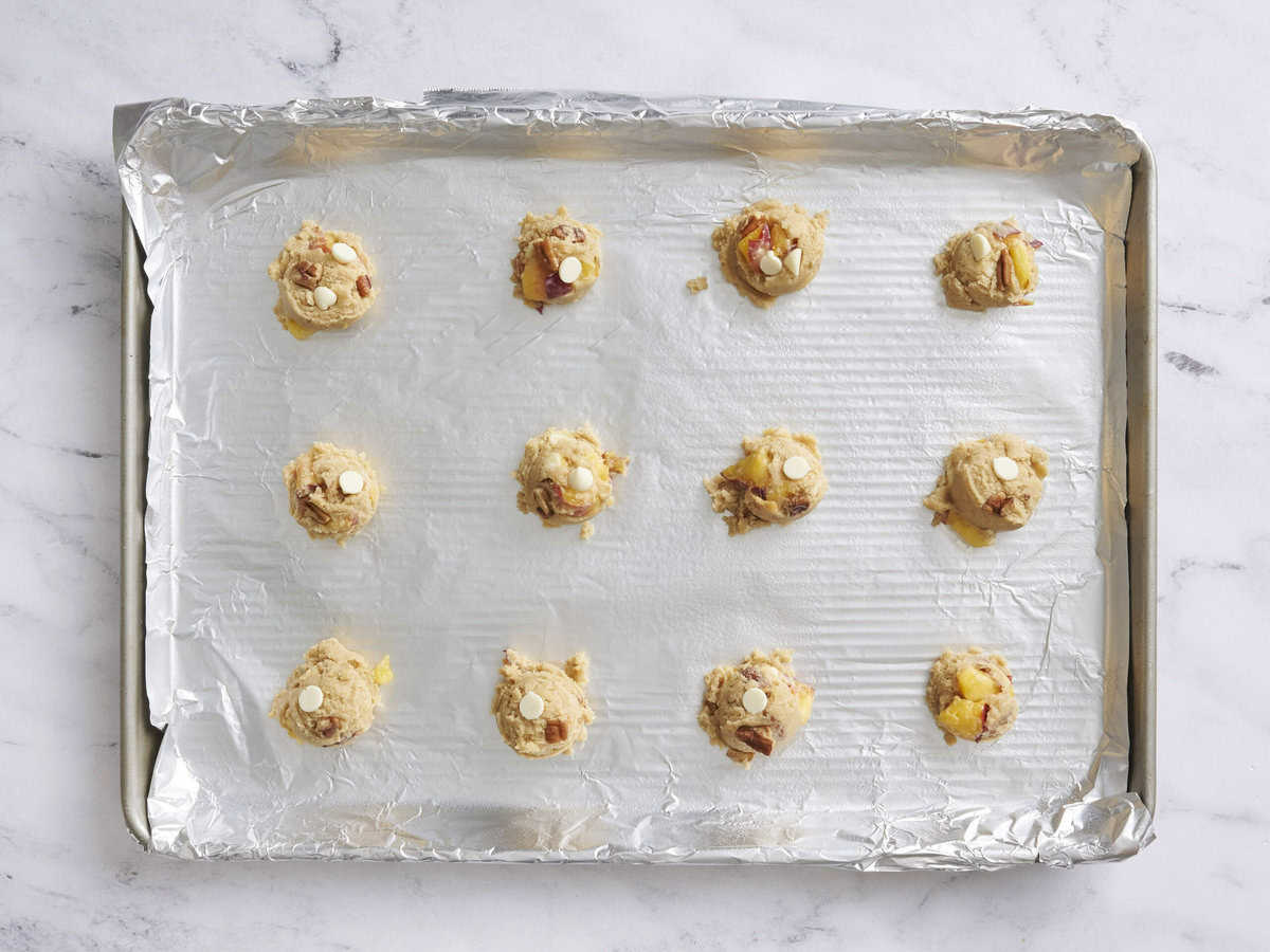 Scoops of peaches and cream cookie dough on a baking sheet.