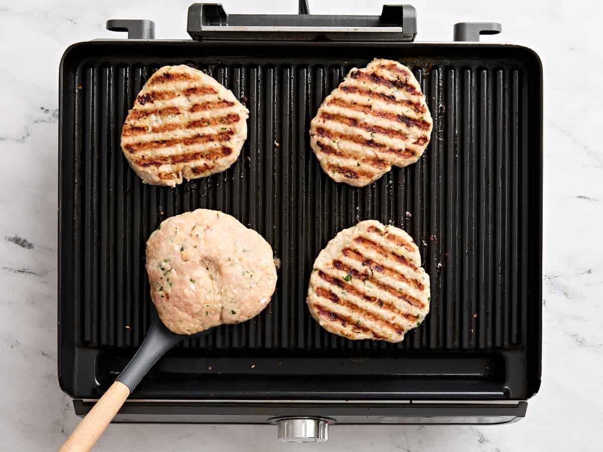 A spatula flipping chicken burgers over on a grill.