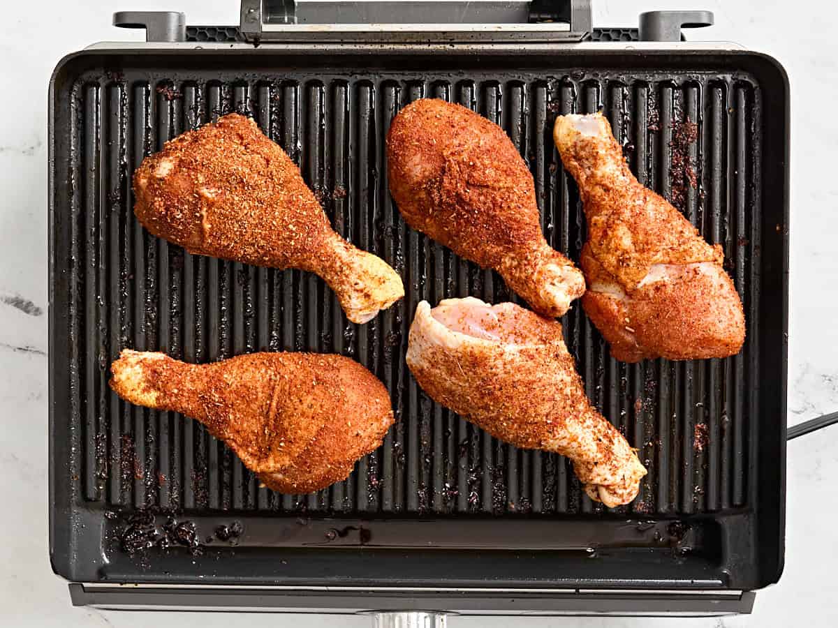 Dry rubbed chicken drumsticks on a grill.