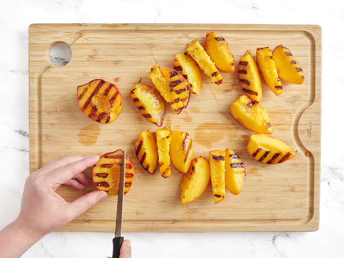 Grilled peaches being sliced on a wooden cutting board.