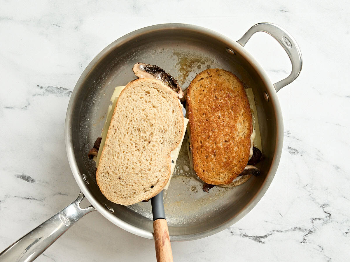 A spatula flipping a mushroom patty melt in a skillet.
