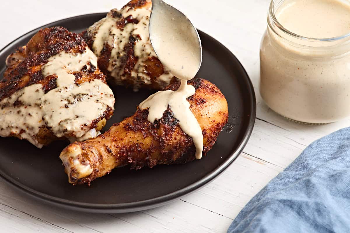 Alabama white sauce being spooned over a grilled chicken drumsticks.