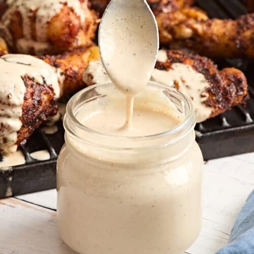 Homemade alabama white sauce in a glass mason jar with a spoon being pulled out covered in sauce.
