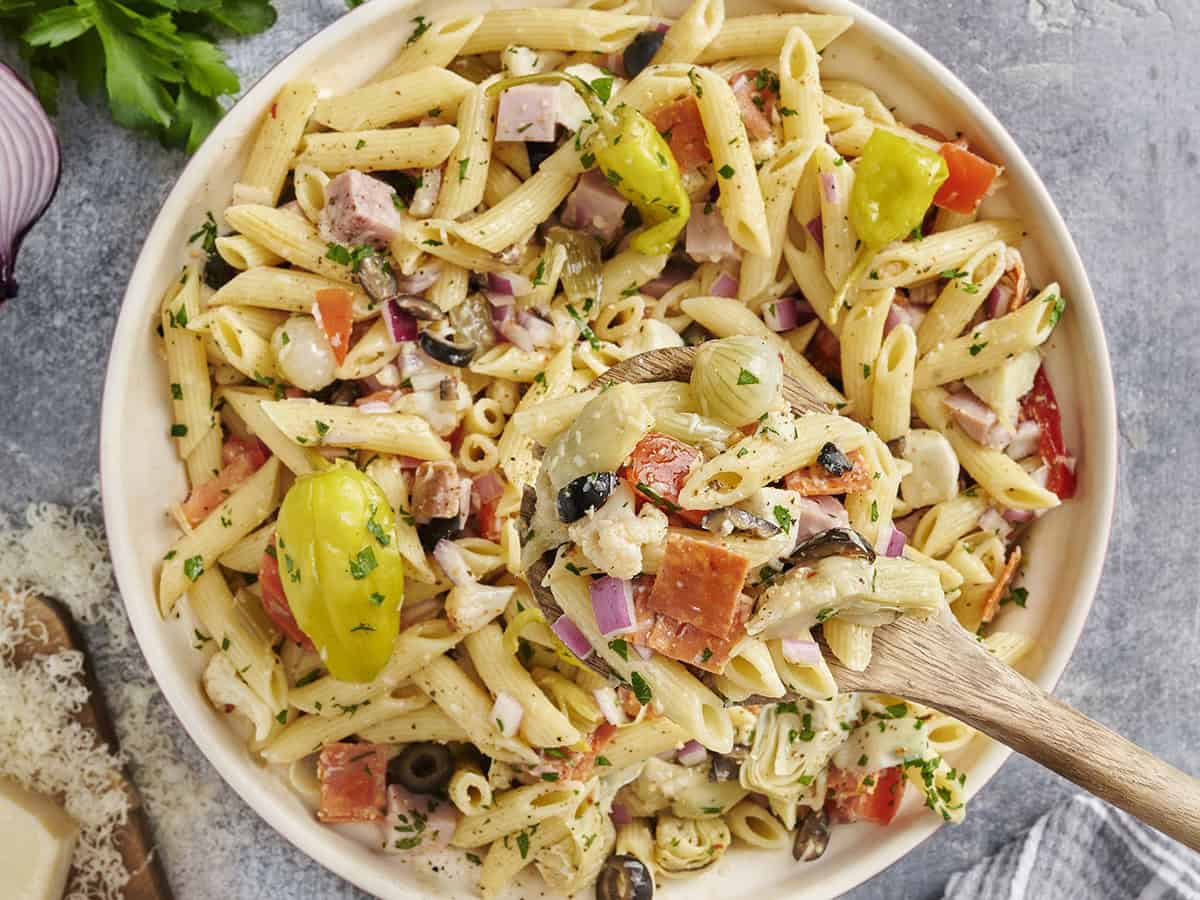 Overhead view of a bowl of antipasto pasta salad with a wooden spoon taking some.