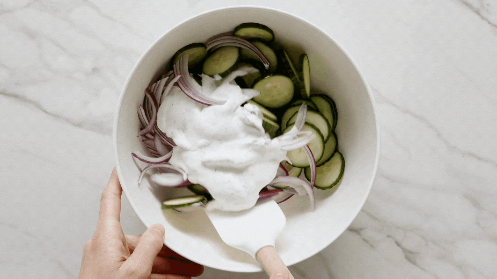 Finished cucumber salad in a bowl with a spatula.