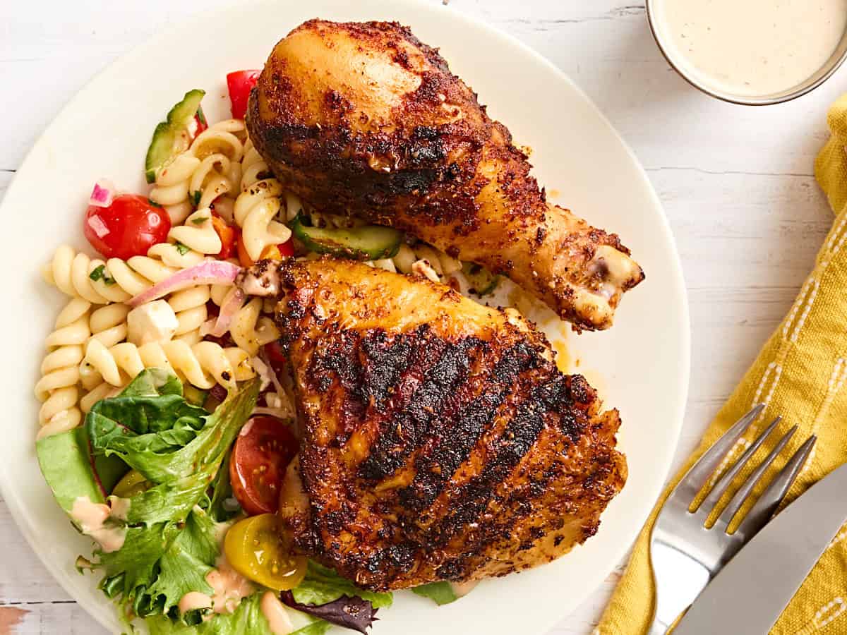 Overhead view of grilled chicken drumsticks and thighs on a plate with pasta salad.