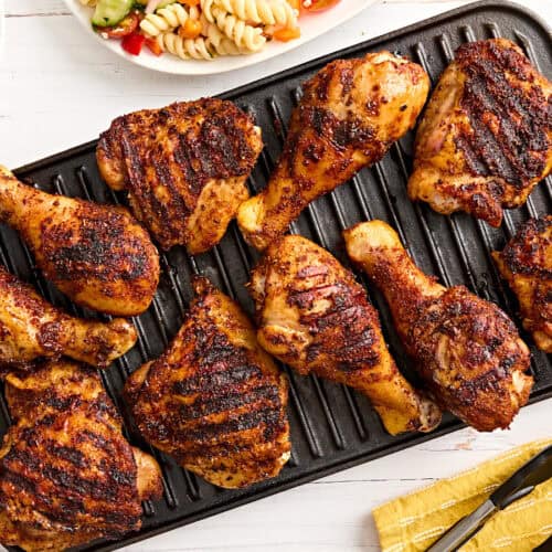 Dry rubbed grilled chicken drumsticks and thighs on a grill.