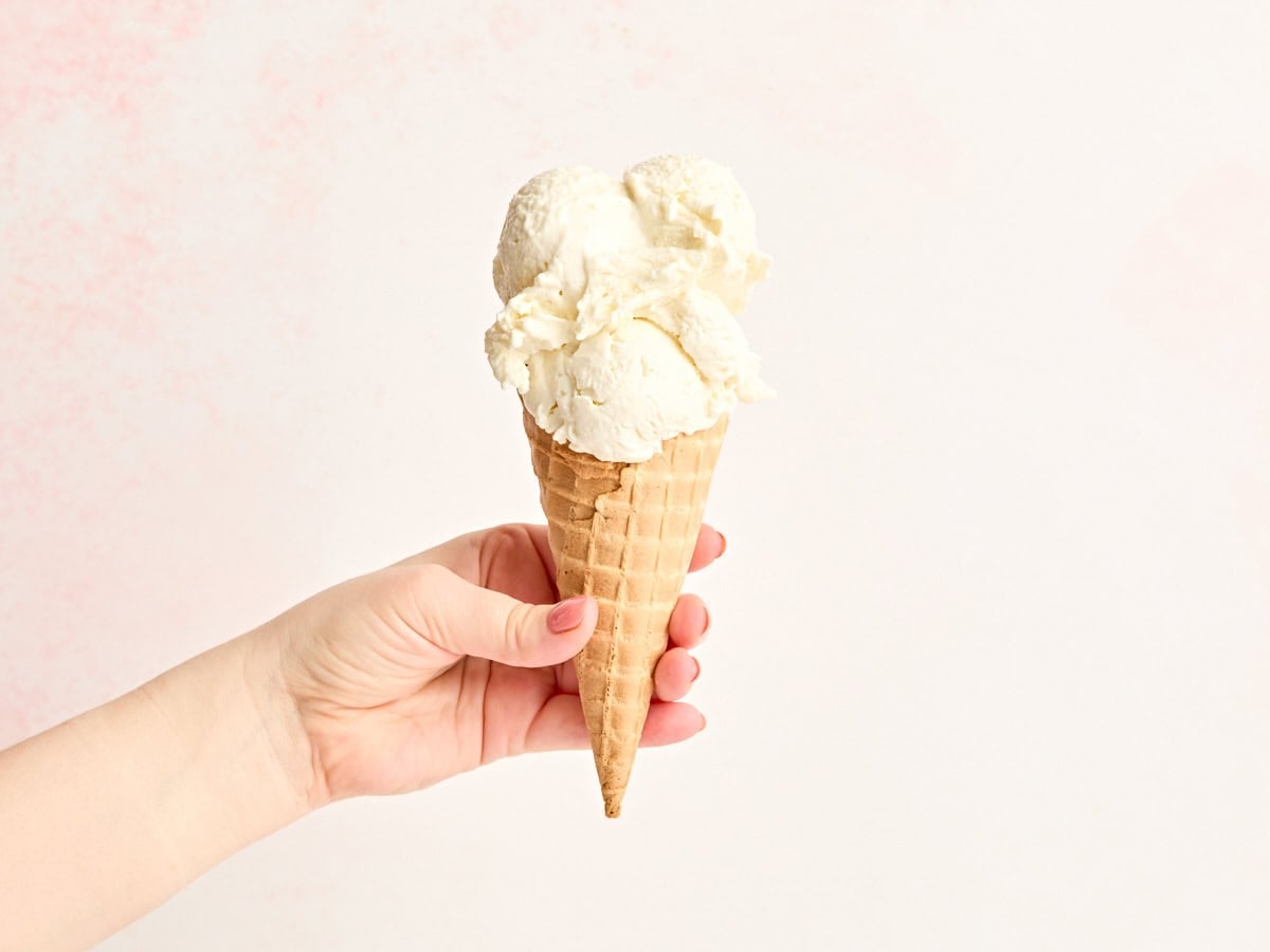 Side view of a hand holding frozen yogurt in a waffle cone.