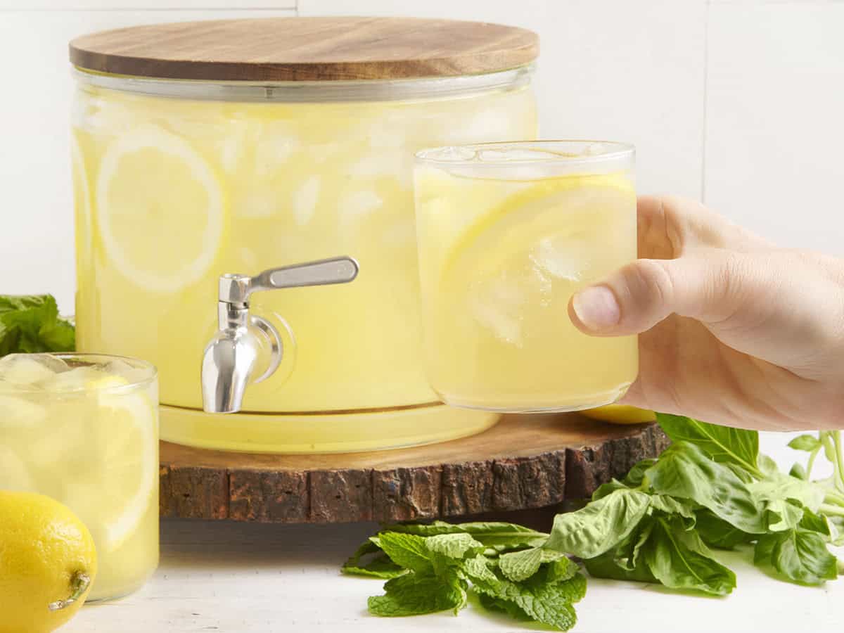 A drink dispenser with fresh lemonade and a hand holding a glass.