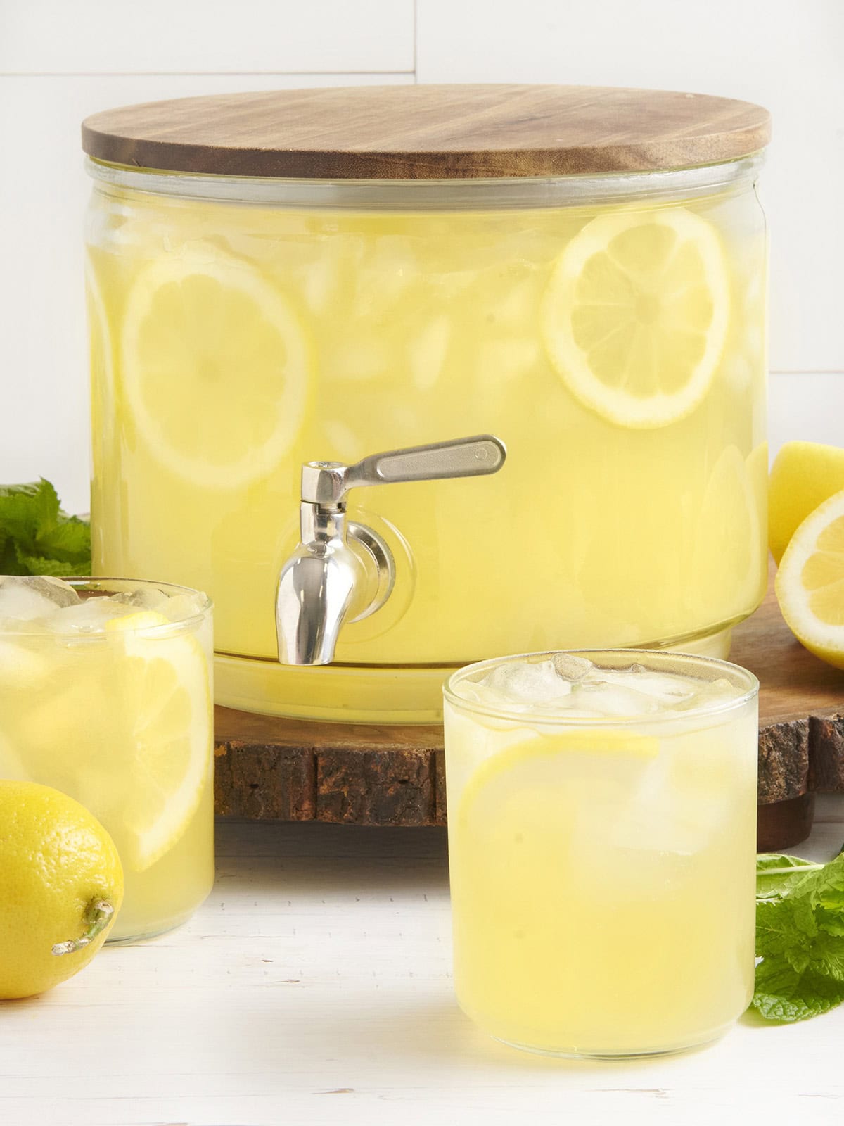 A drink dispenser with homemade lemonade and two glasses of lemonade in front.