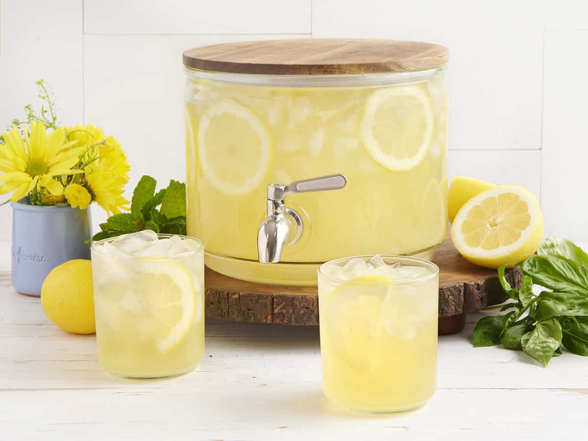 A drink dispenser with homemade lemonade and two glasses of lemonade in front.