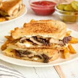 Side view of a mushroom patty melt and fries on a plate.