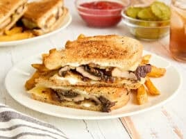 Side view of a mushroom patty melt and fries on a plate.