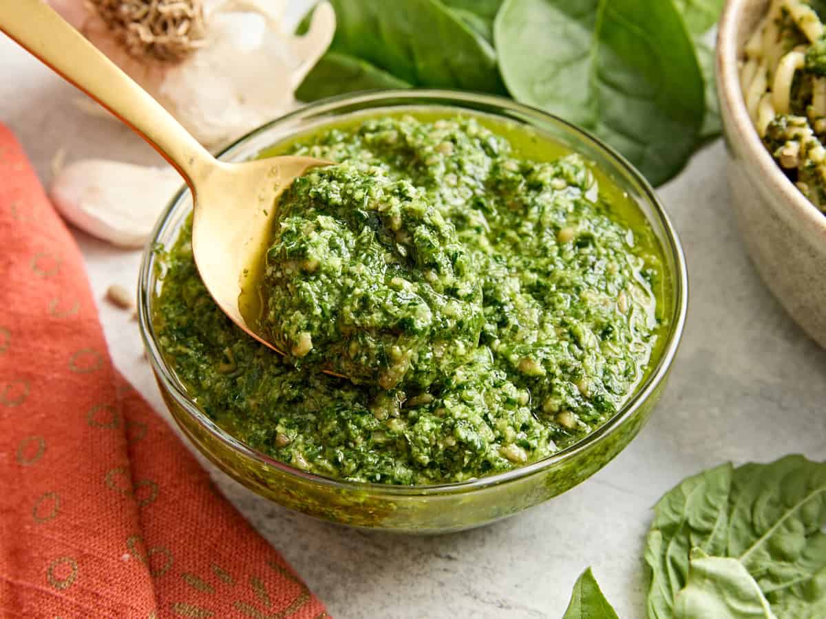 Side view of a bowl of homemade basil pesto with a spoon taking some.