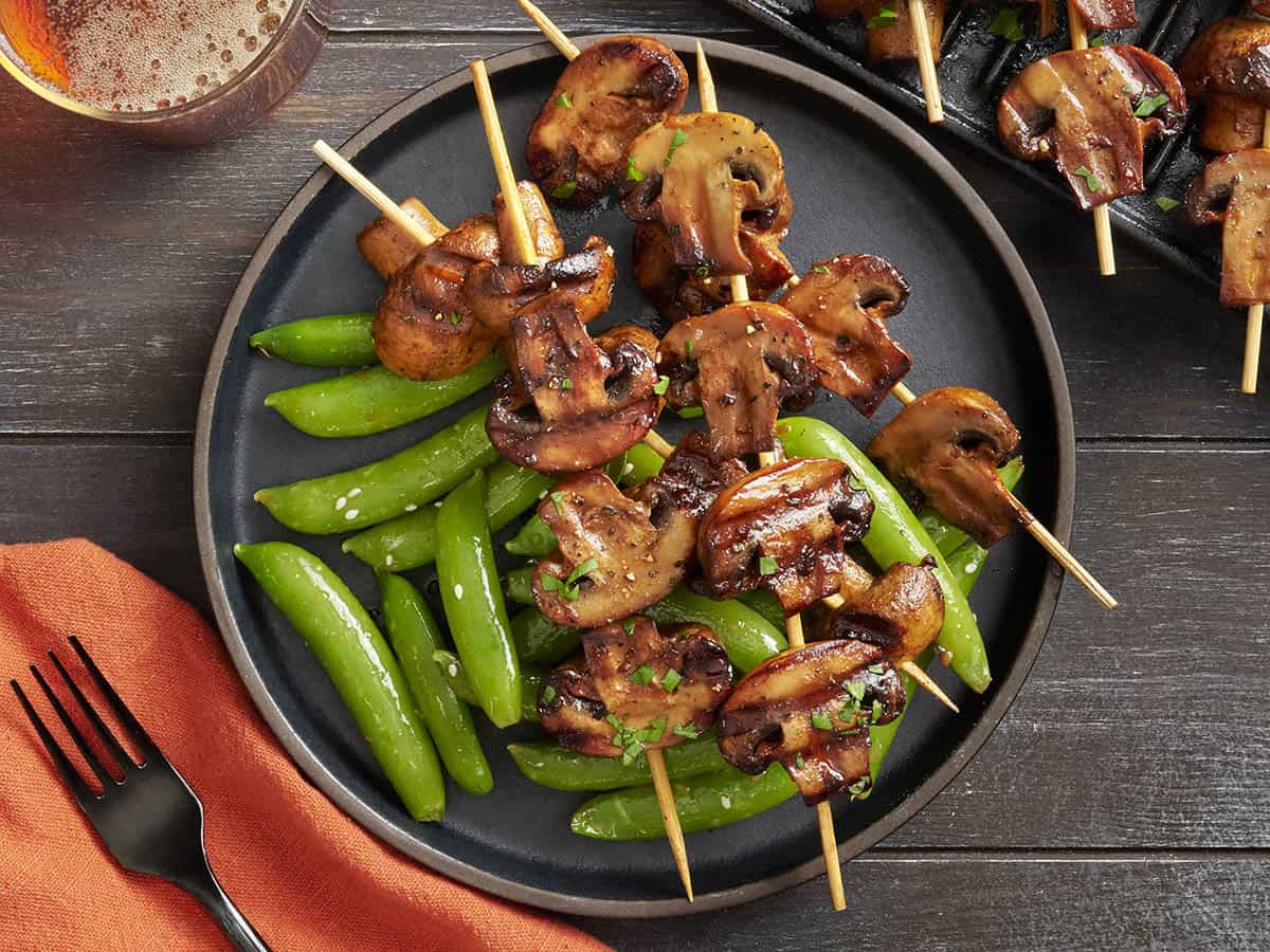 Overhead view of grilled mushroom kebabs on a plate with sugar snap peas.
