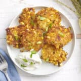 Overhead view of sweet corn fritters on a plate with sour cream and green onions.