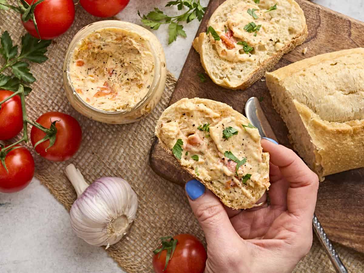 Overhead view of a hand holding a slice of bread topped with tomato butter.