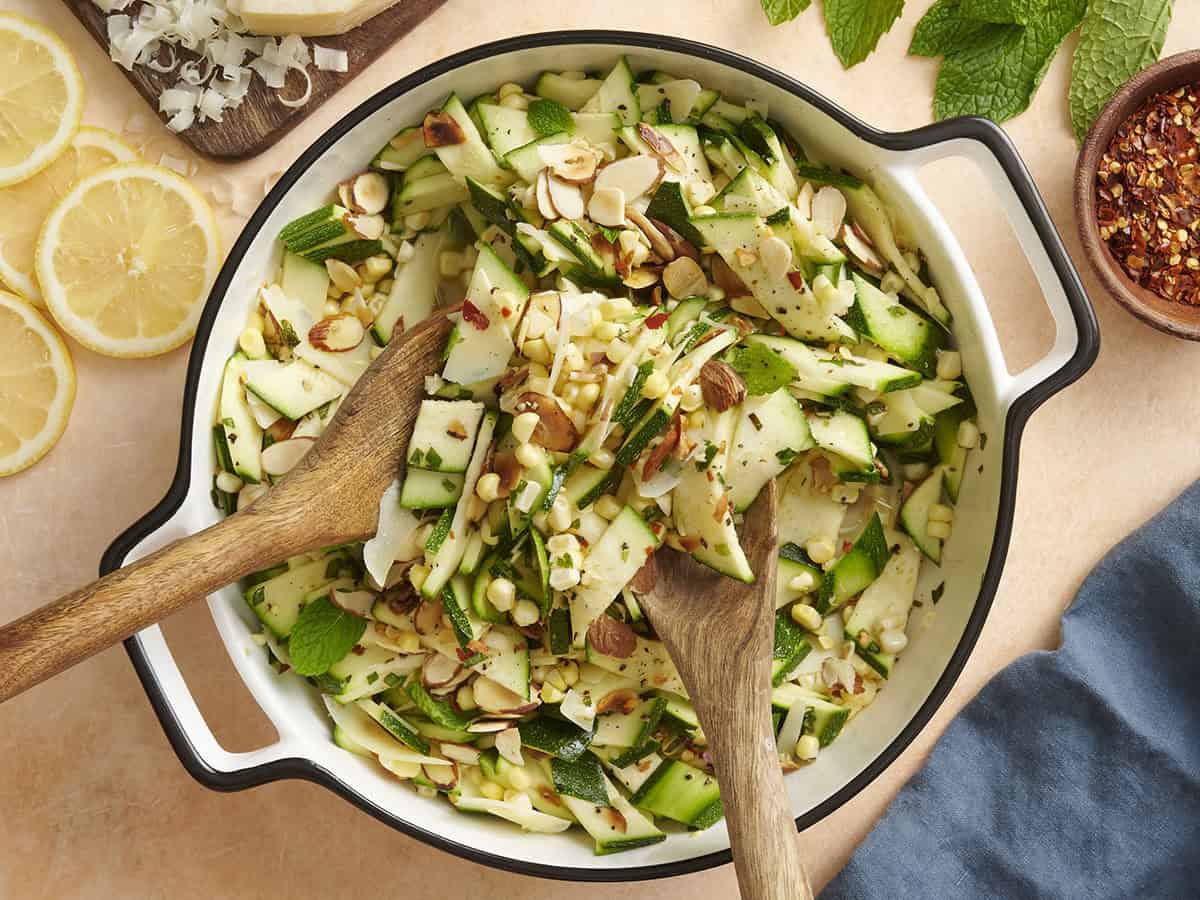 Overhead view of a bowl of zucchini, corn and toasted almond salad with serving spoons taking some.