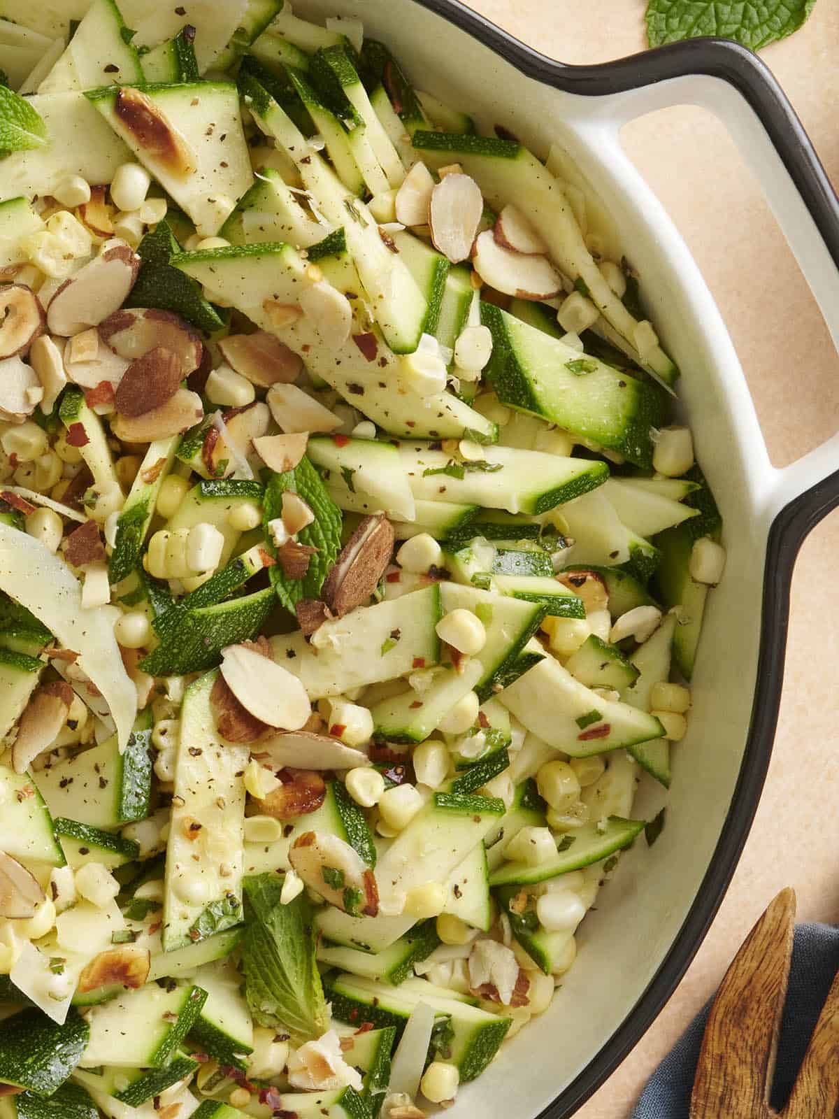 Overhead close up view of a bowl of raw zucchini, corn and toasted almond salad.