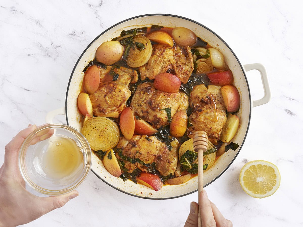 A hand drizzling honey over Braised Chicken and Peaches in a skillet.