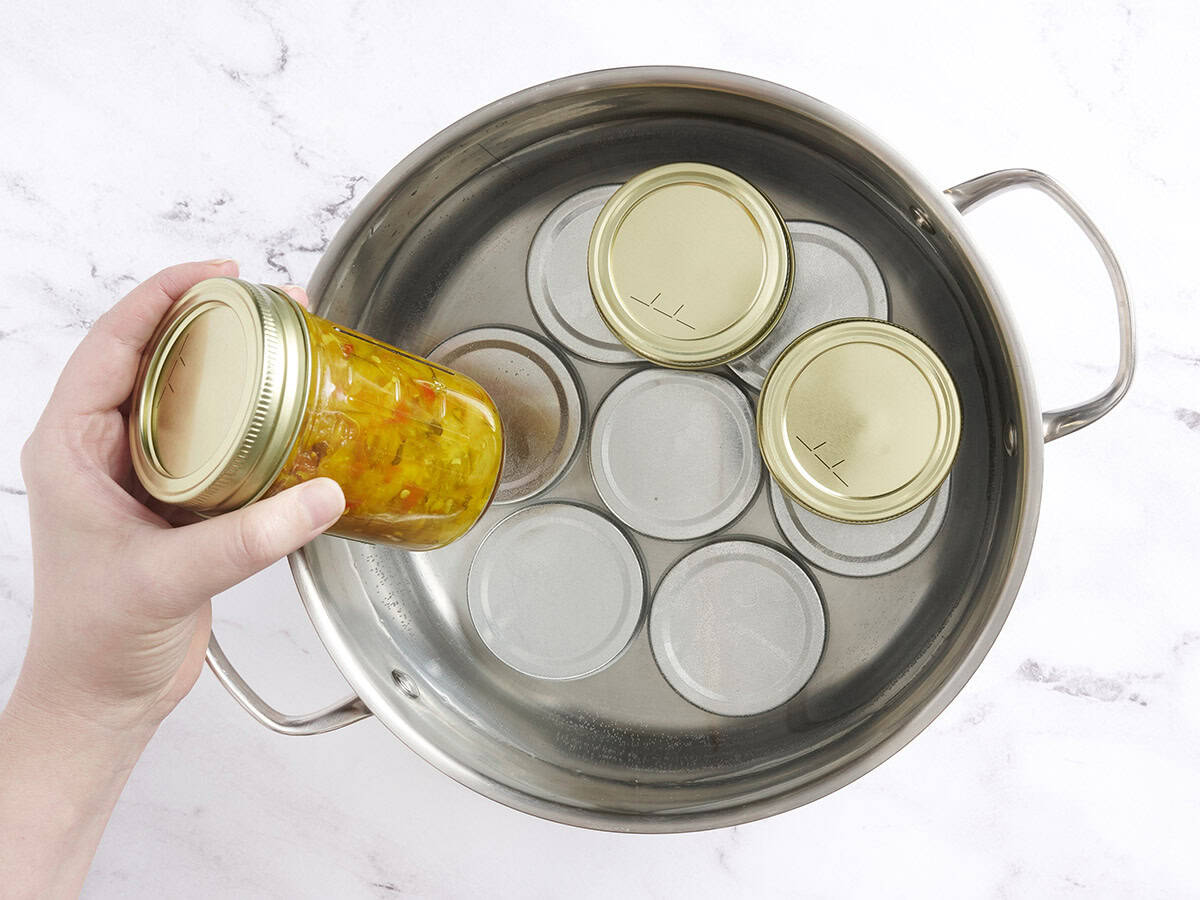 Jars of zucchini relish added to a saucepan.