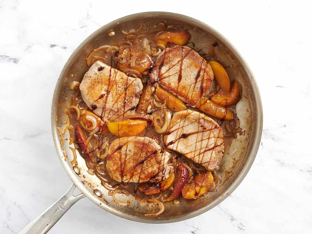 Summer peach pork chops in a skillet drizzled with balsamic glaze.